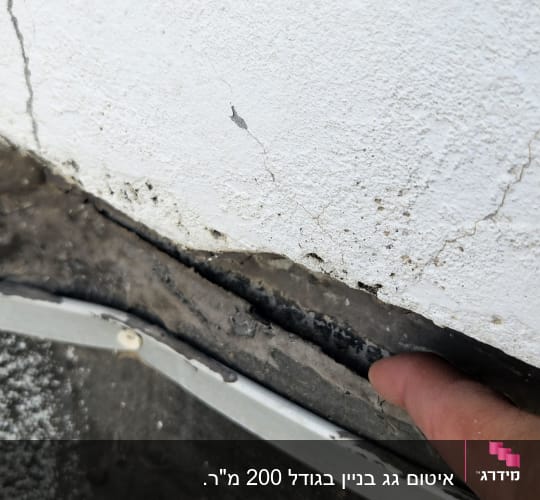 אצבע מצביעה על סדק בקיר עם חומר איטום